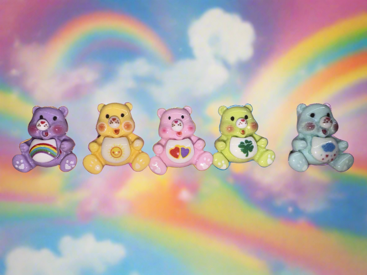 Colorful Care Bear nail charms set against a rainbow background, enhancing manicure style.