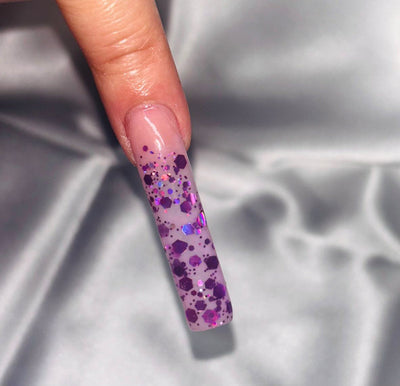 Acrylic nail with purple glitter from the Haunted Hayride collection, showcasing a Halloween theme on a shiny surface.