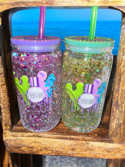 Two sparkly Drip Lab Branded Hot Girl Tumblers with rhinestone lids and colorful straws on a wooden shelf by the water background