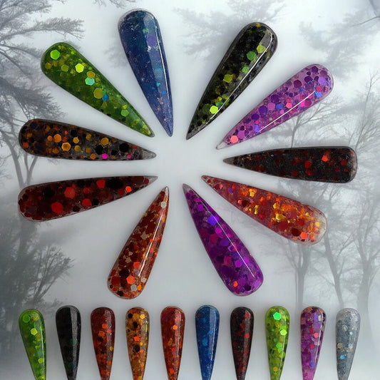 Halloween-themed long stiletto acrylic nails in various glittery colors including green, purple, red, orange, and blue arranged in a circle on a spooky forest background